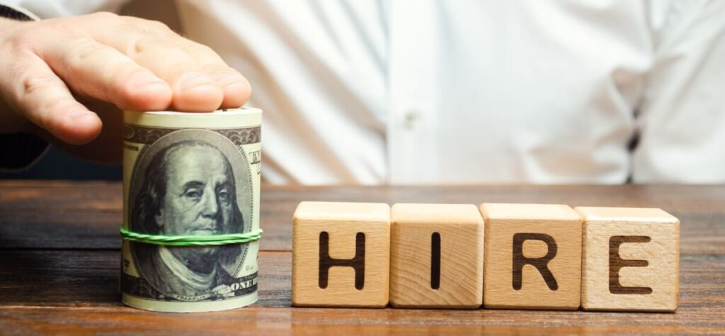 Roll of money next to wooden blocks that spell HIRE